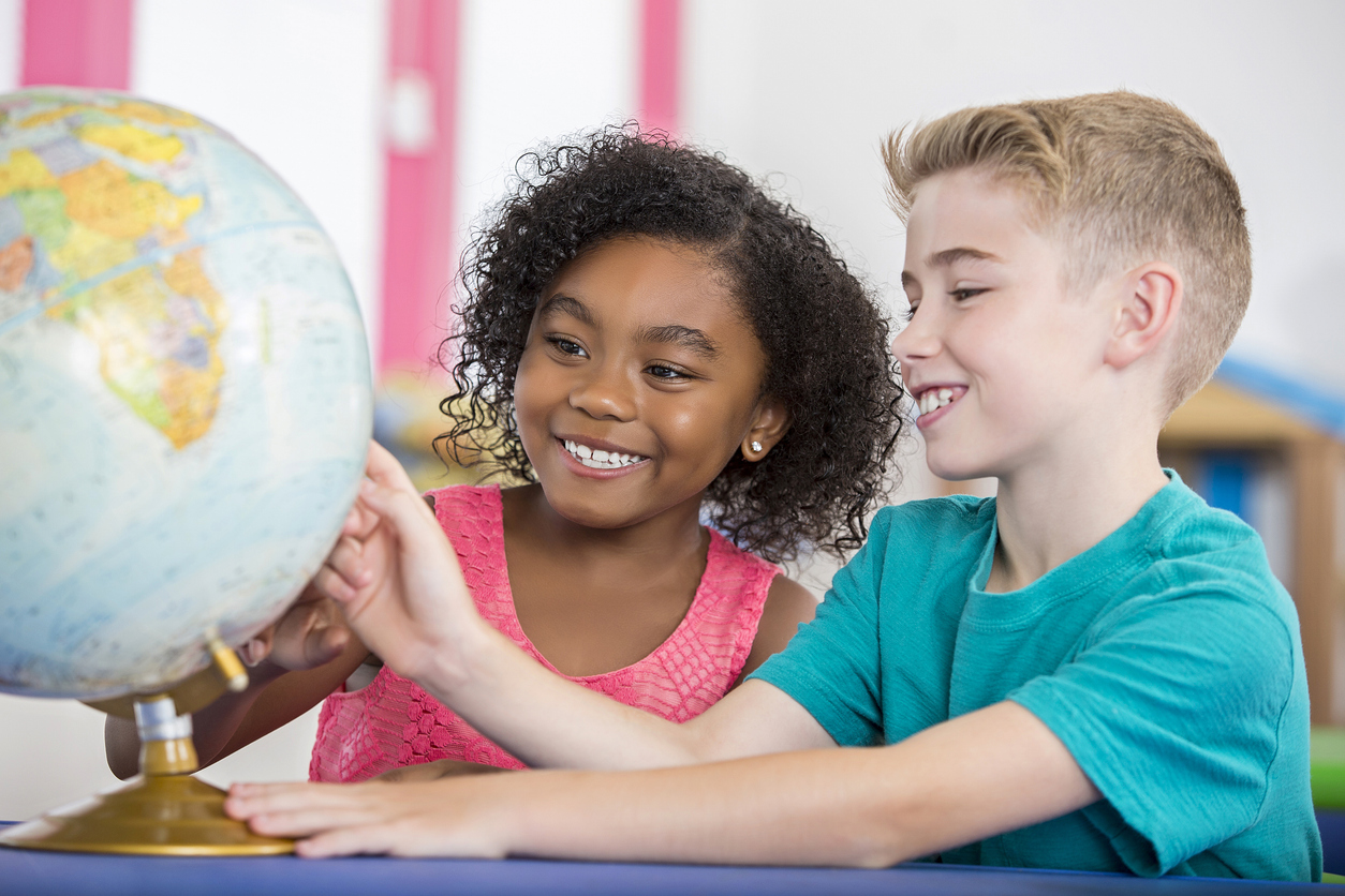 Kaksi eritaustaista lasta katsoo yhdessä maapalloa.