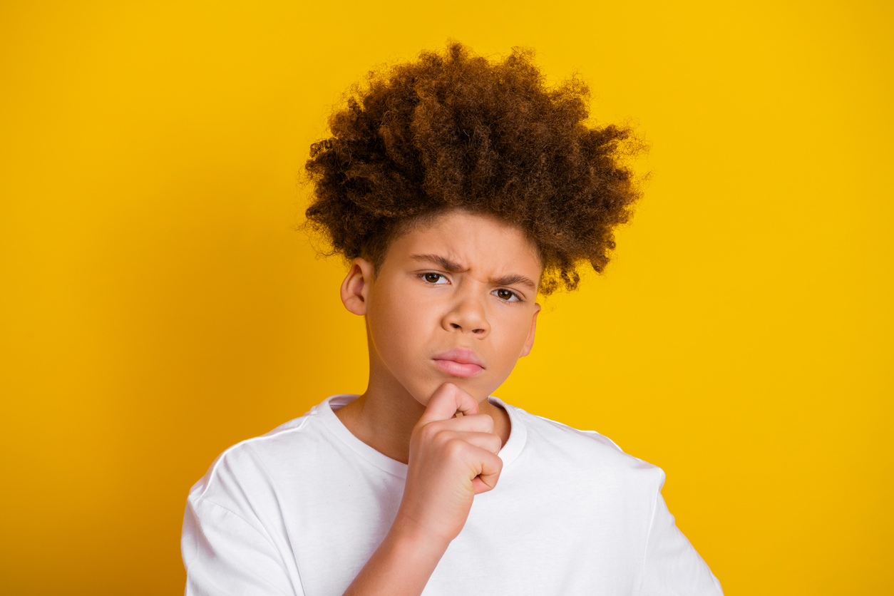 Pohdiskeleva, kiharahiuksinen teinipoika keltaista taustaa vasten.