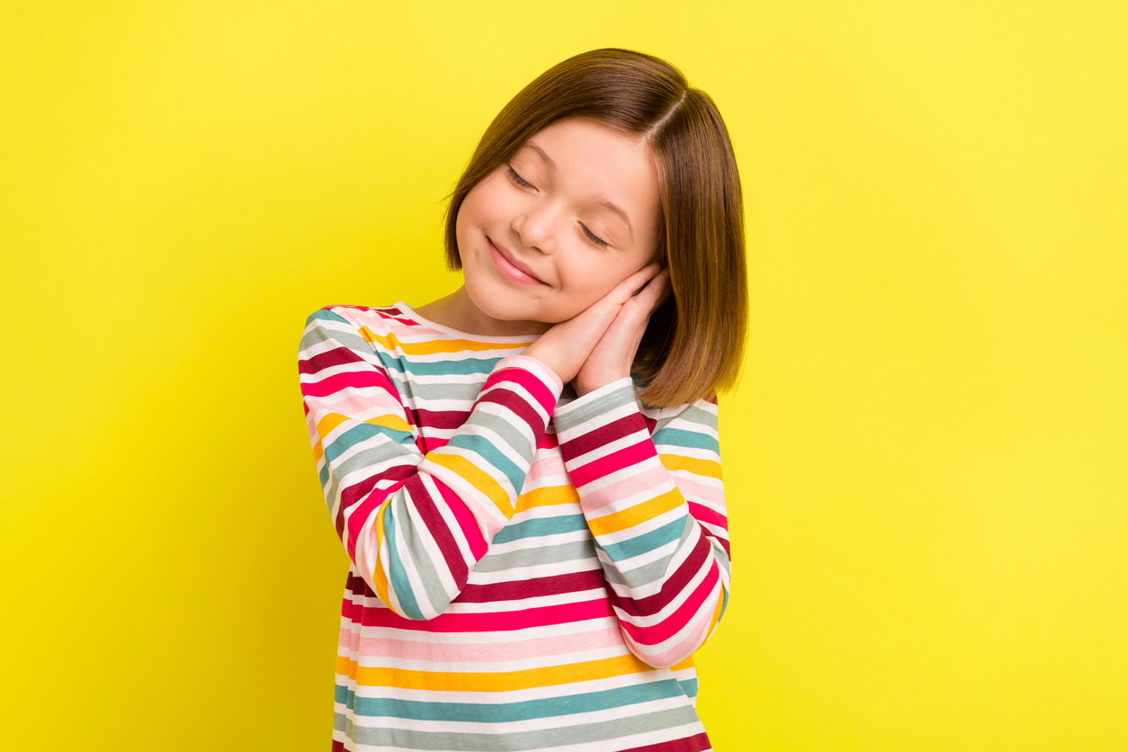 Tyttö pitää käsiään pään vieressä ja näyttää nukkuvalta keltaista taustaa vasten.