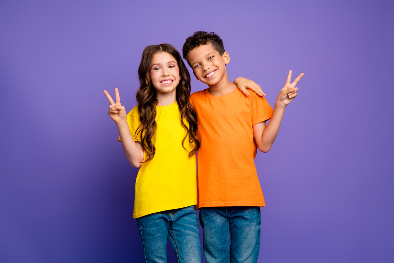 Tyttö ja poika näyttävt rauhanmerkkejä ja pitävät käsiään toistensa ympärillä violettia taustaa vasten.