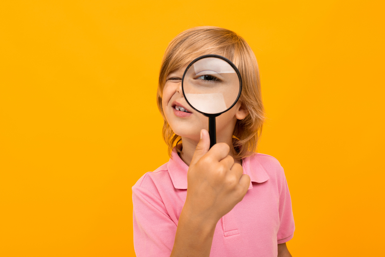 Pieni lapsi katsoo suurennuslasin läpi oranssia taustaa vasten.